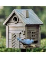 Boomklever eet vogelvoer bij de Multiholk Green Umber van Wildlife Garden, een bruingroen houten nestkast en voederhuis met ronde invliegopening, sierdeur en voederplek met zitstokjes.