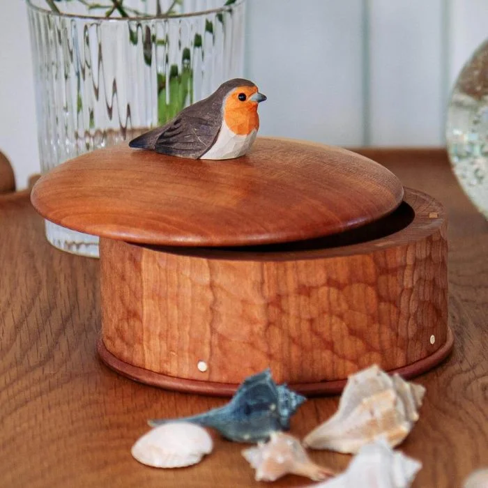 Houten opbergdoos Roodborstje van Wildlife Garden met ronde deksel en houten roodborstje, gefotografeerd op een tafel met schelpen en glazen vaas.