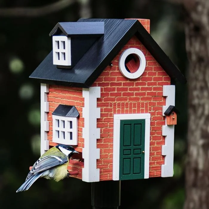 Koolmees bij de voederopening van de Multiholk Brick Cottage van Wildlife Garden, een houten nestkast en voederhuis met rode baksteenlook, groene deur en zwart dak.